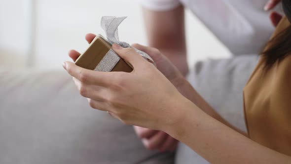 Close up hands Asian man giving a gift box to girlfriend while sitting on the sofa at home.