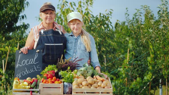 Portrait of a Grandmother with Her Granddaughter Behind the Counter of a Farmers Market Selling alt