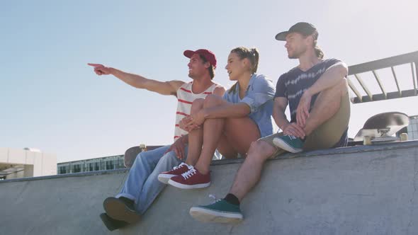Caucasian woman and two male friends sitting talking and pointing something in distance on sunny day alt