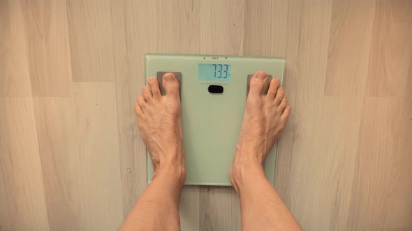 Man On Scales Measure Weight.Guy Legs Step On Bathroom Scale.Diet Man Feet Standing Weighing Scales alt
