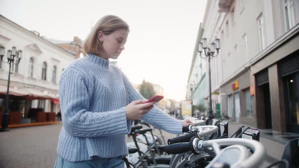 Bicycles for rent in the city center. Woman takes bike bicycle in sharing parking lot. alt