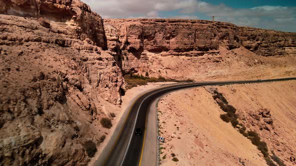 Car Driving on Asphalt Road Through the Desert Sands of the Blue Sky White Clouds