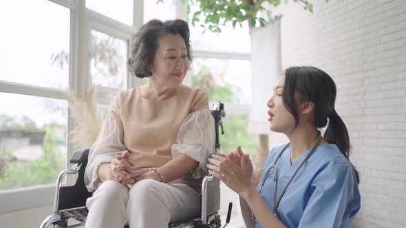 Young Asian nurse talking to a smiling senior female patient on a wheelchair and comforting her.
