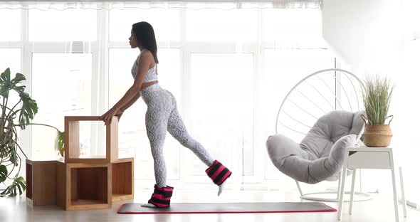 Pretty fitness black woman in sportswear practicing donkey kick exercise with ankle weight.
