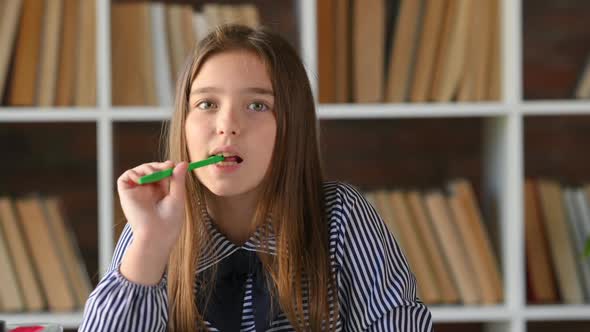 Portrait of Young schoolgirl sitting at table desk with a pen in her hands ponders over the task.