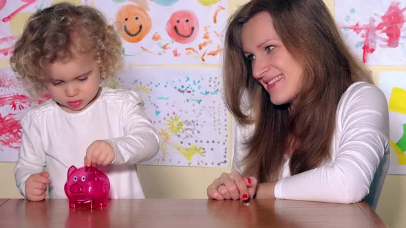 Woman with Kid Putting Coins in Piggy Bank and Show Finger Up Looking at Camera