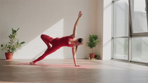 Young Woman in Red Sports Uniform Does Vasisthasana in Yoga Studio alt