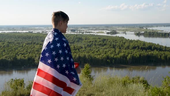 Blonde Boy Waving National USA Flag Outdoors Over Blue Sky at the River Bank