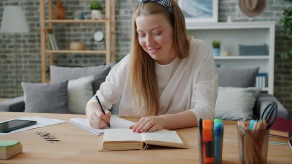 Young Lady Student Writing in Notebook at Desk at Home Working at Project alt