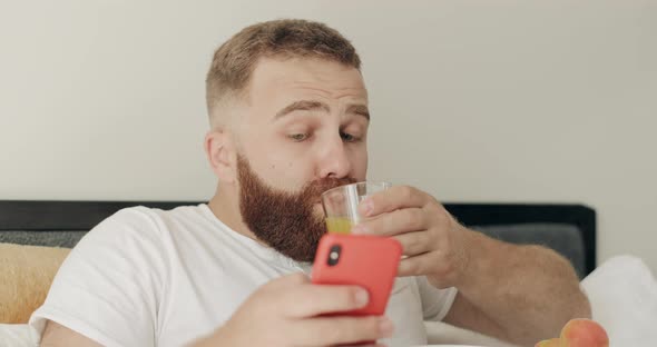 Close Up View of Bearded Young Man Choking on Juice While Reading Shocking News on Smartphone alt