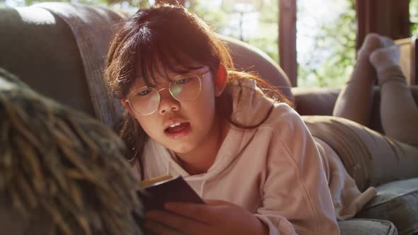Asian girl smiling while reading a book while siting on the couch at home alt