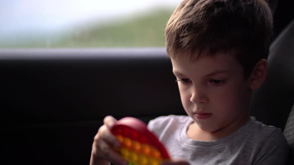 Child Boy Playing with Rainbow Popit or Simple Dimple in Car