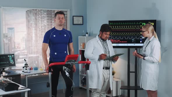 Two Mixed Race Doctors Discussing EKG Data of Athlete Doing Treadmill Test in Sports Lab alt
