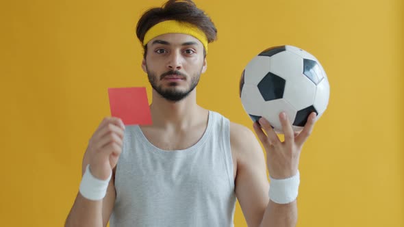 Slow Motion Portrait of Attractive Arab Guy Holding Football Showing Red Card alt