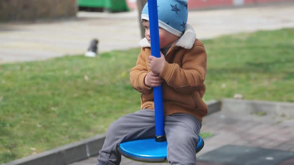 A Boy on a Playground in an Autumn Park Rides on a Swing in Cloudy Weather alt