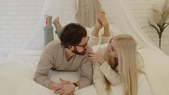 Young Entrepreneur and His Beautiful Businesswoman Girlfriend Laying Down on Their Bed Being Playful alt