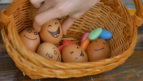 Stack of Eggs with Hand Drawn Faces on Straw Basket with Colorful Candy Easter Preparation Holiday alt