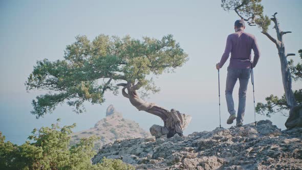 Slow Motion View From the Back of a Middleaged Man with a Camera Approaches the Edge of a Cliff in a alt