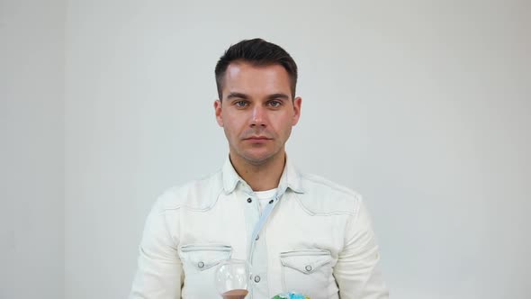 Man Standing on white Background and Posing on Camera with Small Globe and Sand Clock in His Hands alt
