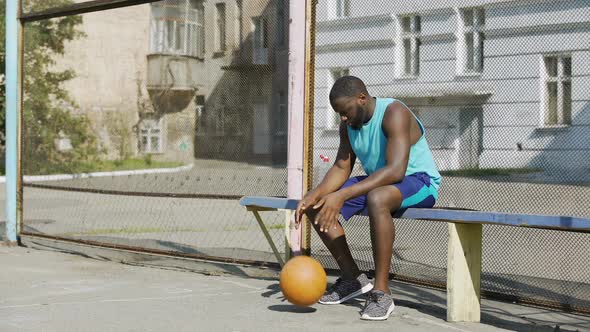 Lonely Afro-American Sportsman sitting on bench and playing with ball