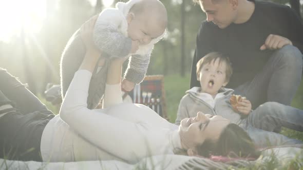 Side View of Happy Young Beautiful Woman Playing in Sunlight with Cute Infant As Handsome Caucasian alt