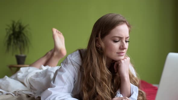 Young Girl Uses Laptop While Lying On Bed In Apartment alt