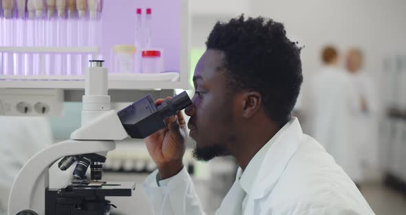 Africanamerican Man Making Medical Research Using Microscope Working in Lab alt