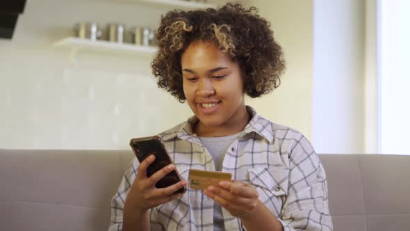A Happy Young AfricanAmerican Woman Pays Through Her Smartphone at Home alt