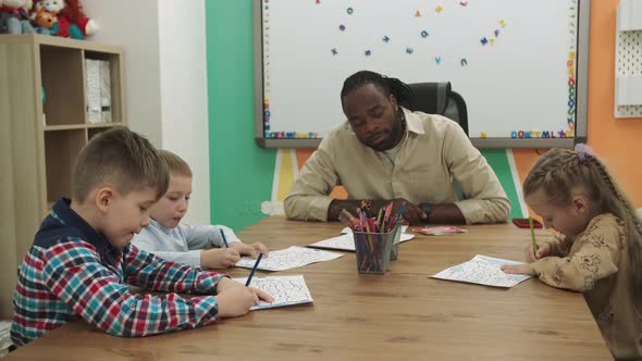 An African American Teacher Teaches a Group of Children to Draw While Sitting at a Table in the alt