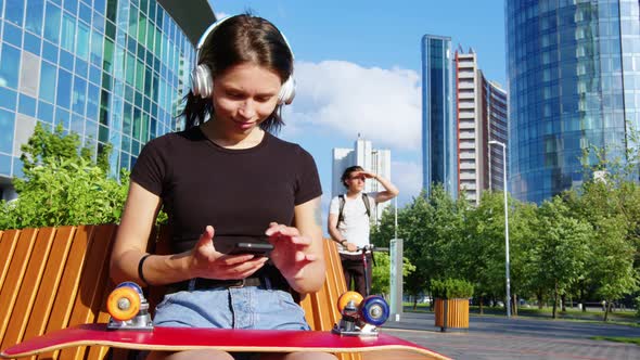 A Girl with a Skateboard Uses a Mobile Phone alt