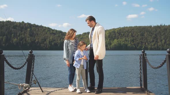 Happy Family Looking at Camera While Posing on Pier at Quiet Lake alt