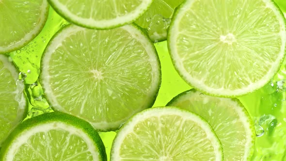 Super Slow Motion Shot of Lime Slices Falling Into Water on Green Background at 1000Fps alt