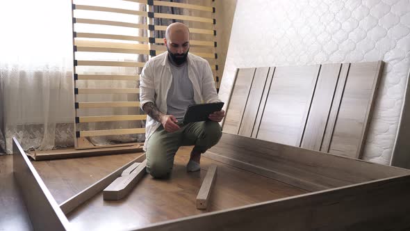 Bearded Man with Tattoo on the Hand with Instruction in the Tablet for Assembling Furniture is Going alt