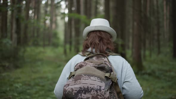 Woman in a Hat and with a Backpack Walks Through the Forest Close Up Back View