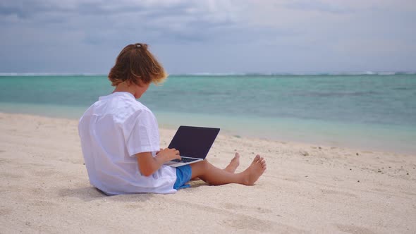 A Student is Engaged in Selfeducation Sitting on the Beach Against the Background of the Turquoise alt