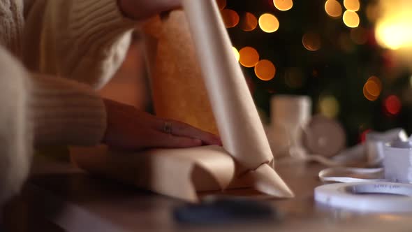Closeup Hands of Unrecognizable Young Woman Wrapping Festive Christmas Gift Box in Craft Paper with alt