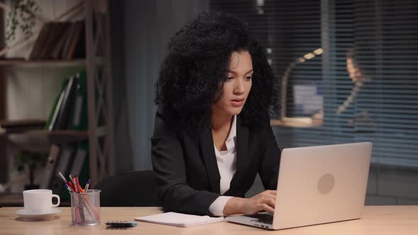 Portrait of African American Woman Looking at Laptop Screen and Making Notes in Notebook alt