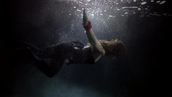 Slim Woman Is Floating Underwater in Darkness and Depth Subaquatic Shot alt