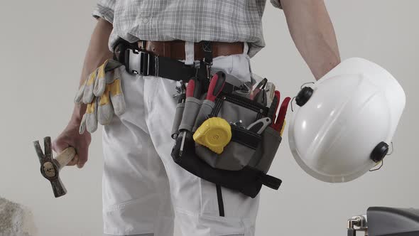 construction man worker wearing a tool bag belt, helmet with headphones and hammer in his hands