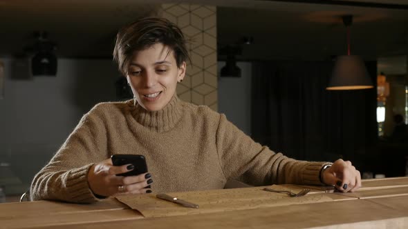 a Lonely Girl Sits in a Restaurant Smiles and Looks at the Phone