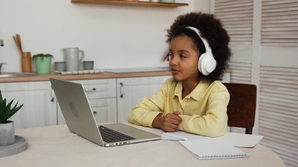 Little African American Girl in Headphones Uses Laptop to Video Call with Teacher alt