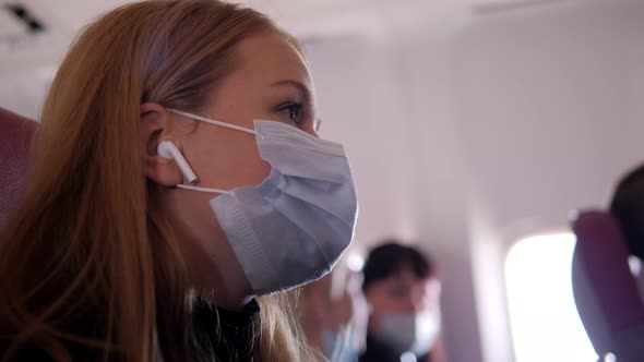 A Woman in a Mask Putting on Wireless Headphones in an Airplane During Flight alt