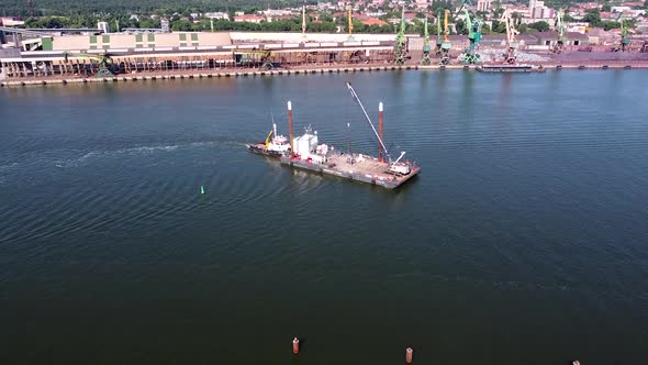 Tugboat pushing barge with view of industrial cranes of Klaipeda harbor, aerial view alt
