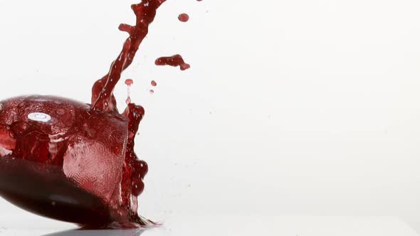 Glass Falling and Red Wine splashing against White Background, Slow Motion