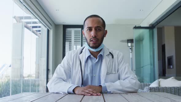 Mixed race male doctor wearing face mask talking during video call alt