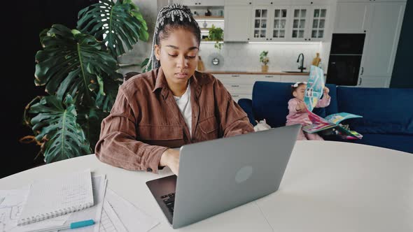 Young Serious African American Woman Entrepreneur Working Online From Home Her Little Daughter alt