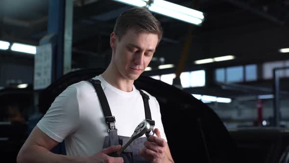 Closeup Portrait of Handsome Young Mechanic Male Wearing Uniform Tightening Nut with Special Key alt