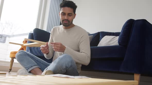 Confused Man In Lounge At Home Reading Instructions For Flat Pack Furniture Assembly