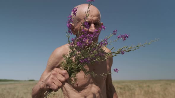 Motion Around Satisfied Old Man Smelling Flowers on Field