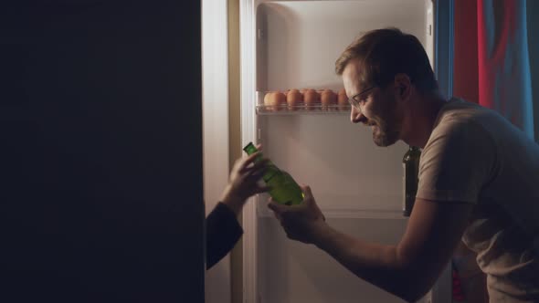 a Man Opens the Refrigerator at Night to Get a Bottle of Beer alt